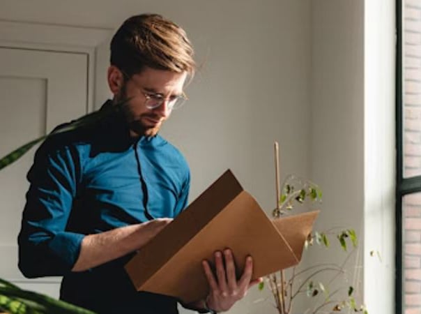 Bookkeeper standing up in a blue shirt reading and analyzing finances. A plant is to the left.