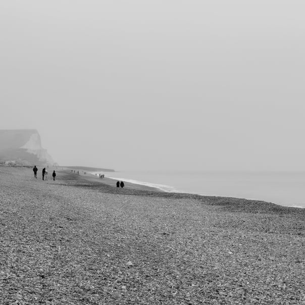 A black & white photo along seaford beach where people are walking along towards the cliffs in the distance