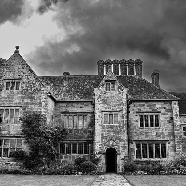 A black & white photos of National Trust Batemans set against stormy looking clouds.