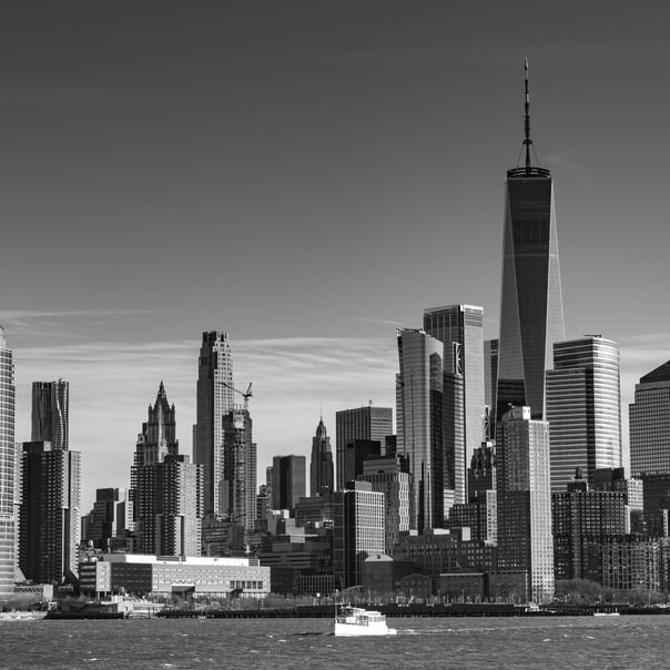 A black and white photo of New York City skyline taken from the Hudson River. in the forground is a pleasure boat passing