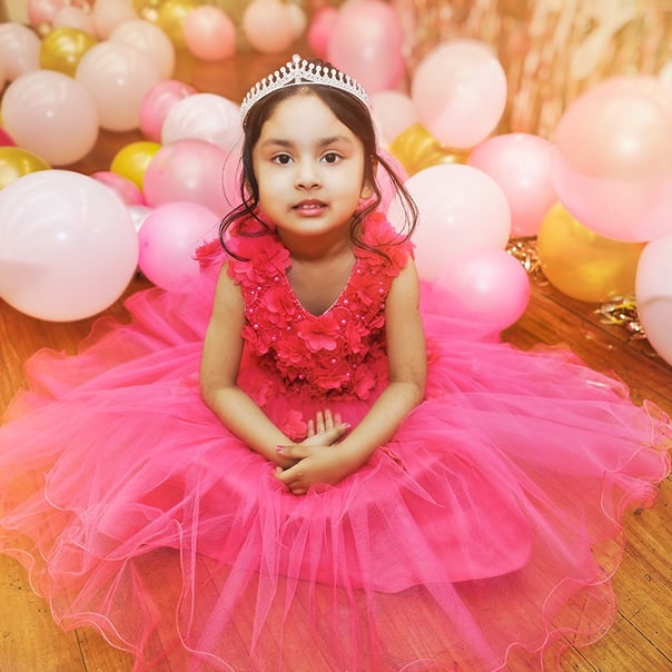 A happy girl wearing a pink princess dress proudly dons a white crown, exuding a regal appearance."
