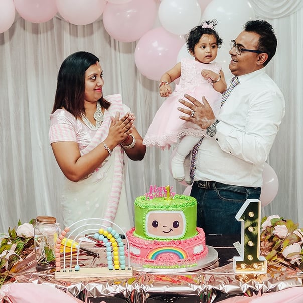 A woman and a man holding a cute baby pose in front of a Cocoomelone-themed birthday cake.