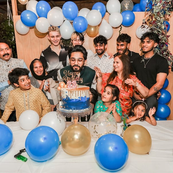 A young man blows out candles on a cake while others cheer and clap in celebration.