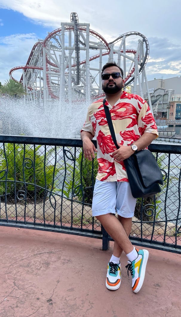 a man in a red shirt and white shorts in front of a roller coaster
