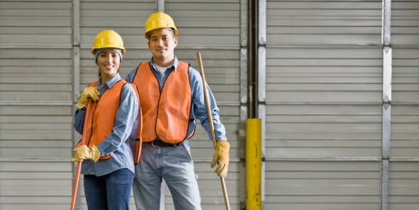 a man and woman in safety vests and hard hats cleaning warehouse