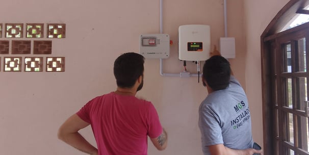 Técnicos em energia solar em frente a display digital de monitoramento fotovoltaico na parede