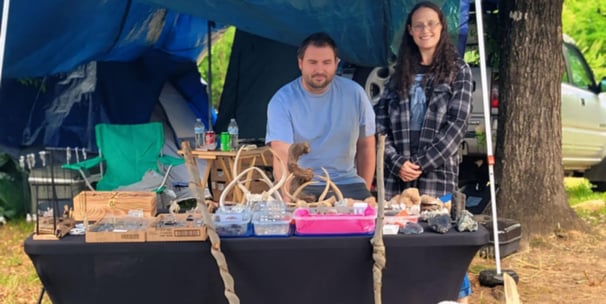 a man and woman standing in front of a vendor table with a variety of rocks and antlers
