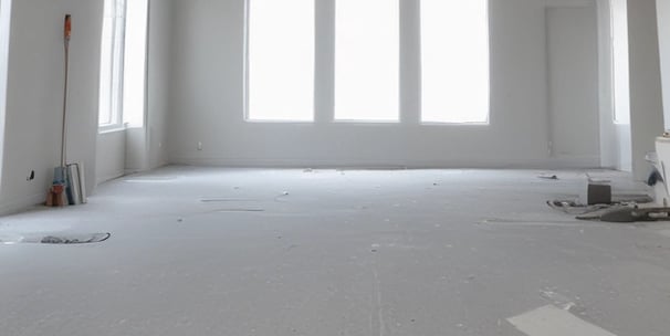 The image depicts a partially renovated or under-construction room. An unfinished wall with visible drywall and joints can be seen, alongside scattered construction materials like a ladder, wooden boards, and yellow construction buckets. A door is propped open, leading to a dimly lit area with more materials stacked in the background.