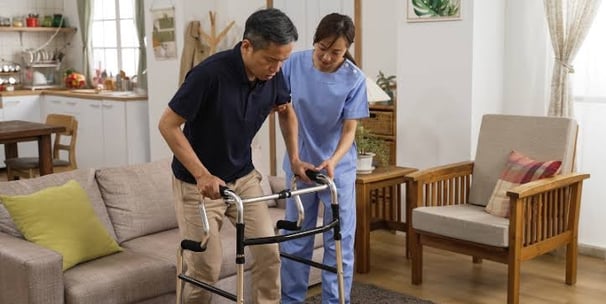 home physiotherapist helping a neurological patient walk using a walker for balance.
