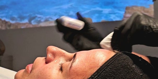 uma mulher deitada em uma marquesa recebendo tratamento facial com uma projeção ao fundo