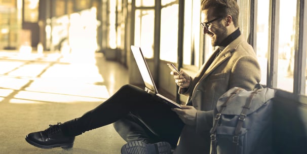 a man sitting on a suitcase and looking at his laptop