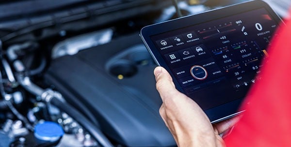 man holding a tablet analyzing a car's engine.