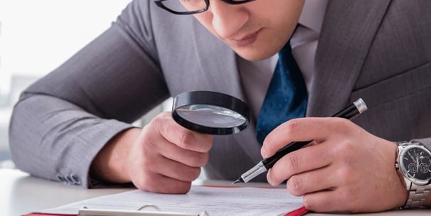 homem com uma lupa inspecionando um documento