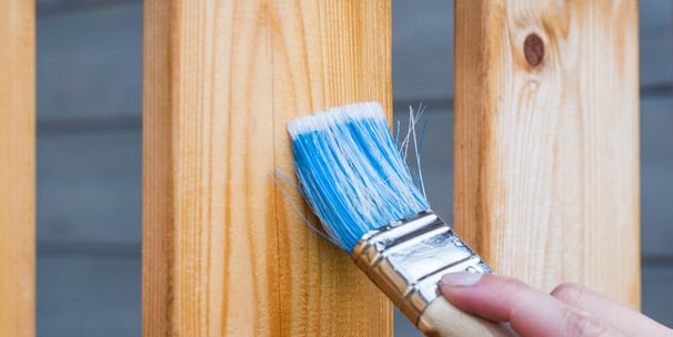 a paint brush putting stain on a wood fence