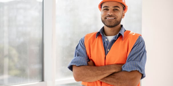 Um engenheiro elétrico usando colete e capacete de segurança sorrindo e com braço cruzado