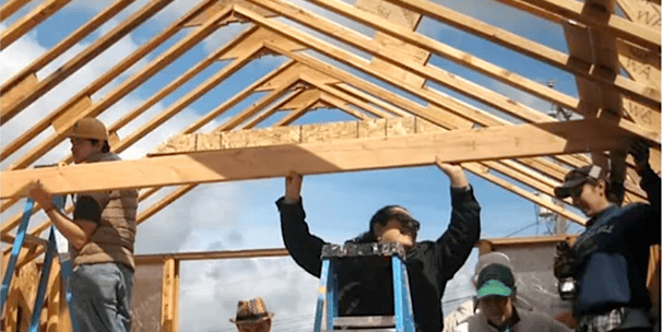 two women and a man framing the trusses of a house construction