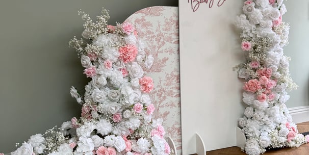 a large pink and white baby shower arch backdrop decorated with flowers