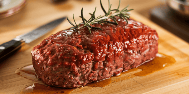 a juicy meatloaf on a cutting board with a knife