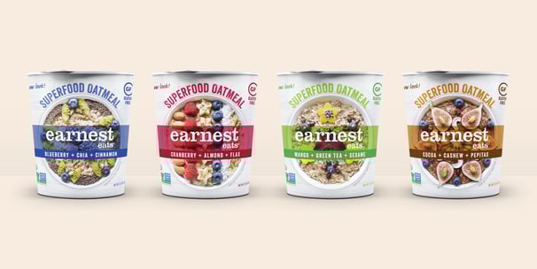 Four 3D mockups of Earnest Eats oatmeal cups side by side on a beige background.
