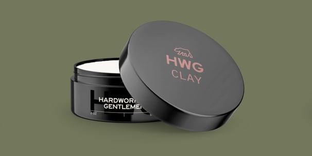 3D mockup of a black Hardworking Gentlemen Clay Pomade plastic container open on a green background.