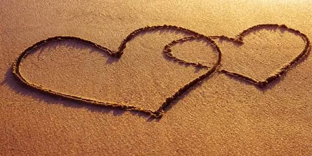 two hearts in the sand with a heart shaped drawing on the sand