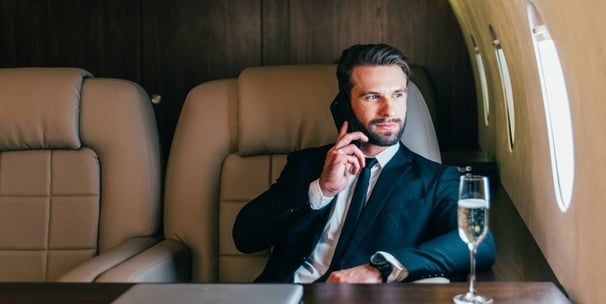 Homem sentado na poltrona do avião na classe executiva ao telefone e degustando um champagne