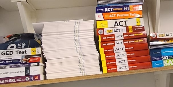 Test prep books on a shelf displaying some of the tests Benny specializes in