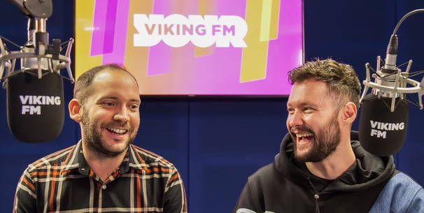Alex Duffy and Calum Scott sit behind microphones in the Viking FM radio studio. Both are laughing.