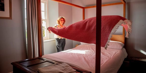 a woman standing in front of a bed with a blanket on it