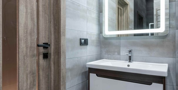 Photo of a modern bathroom vanity with illuminated mirror and grey tiled