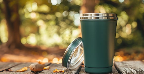 Dark green stainless steel tumbler on a wooden table in an outdoor setting.