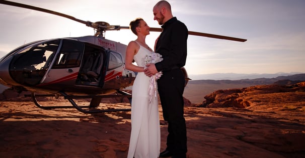 a bride and groom standing in front of a helicopter