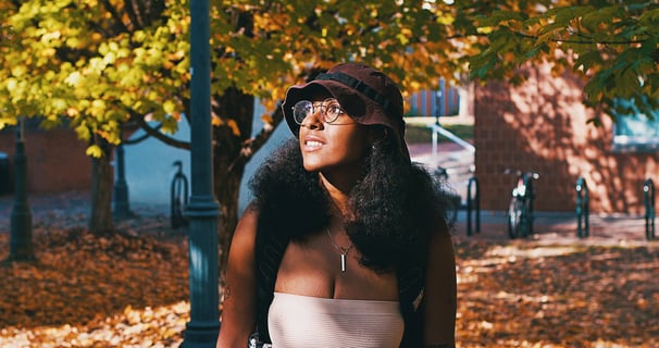 Young college black woman smiling and birdwatching underneath golden yellow autumn trees.