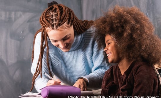 Smiling woman helping a young girl with schoolwork in a warm, supportive setting.