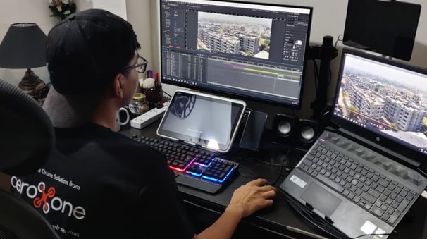 a man sitting at a desk with a laptop and a laptop editing drone video of aeroxone compnay 