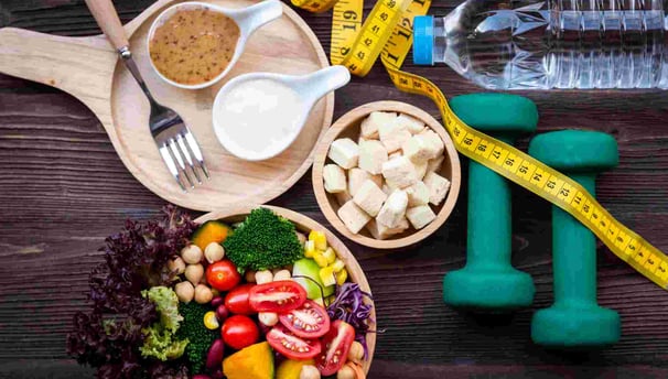 Alimentos saudáveis, fita métrica, halteres e água, representando nutrição e exercício.