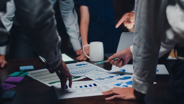 a group of people standing around a table holding papers and discussing
