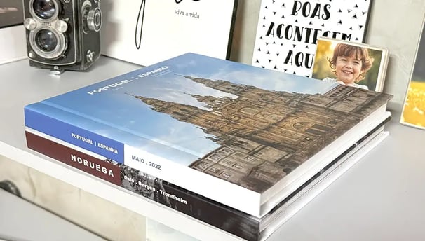 Dois Fotolivros, um sendo da Noruega e ouro de Portual e Espanha. Eles estão sobre uma mesa bem decorada com fotos.