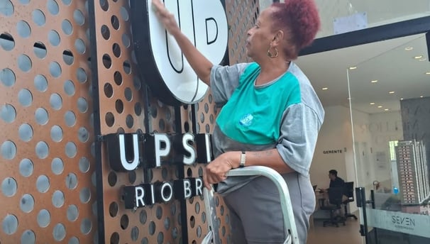 uma mulher limpa uma fachada ela está de camisa cinza com verde