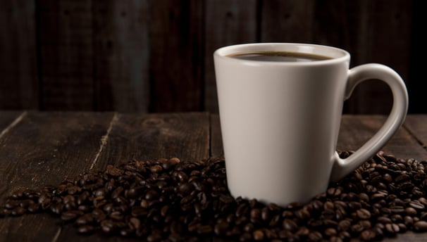 Vista lateral de una taza de café, sobre granos de café en una mesa