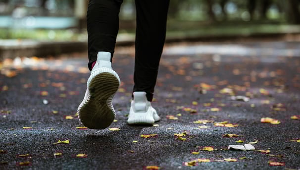 Vista trasera de una persona corriendo, vestida con ropa negra y tenis blancos