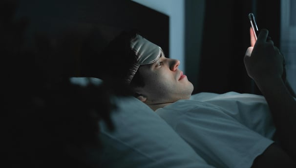 Persona acostada en su cama, revisando su teléfono celular, antes de dormir