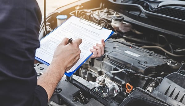 a man in a blue shirt is holding a clipboard and a clipboard evaluating a car's engine.