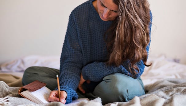 a woman sitting on a bed with a notebook and a pen