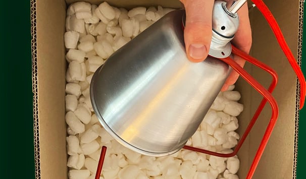 A white hadn't putting a red lamp into a cardboard box full of eco-friendly packing peanuts.