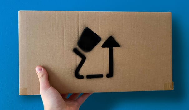 White hand holding up a brown cardboard box with a logo on a blue background