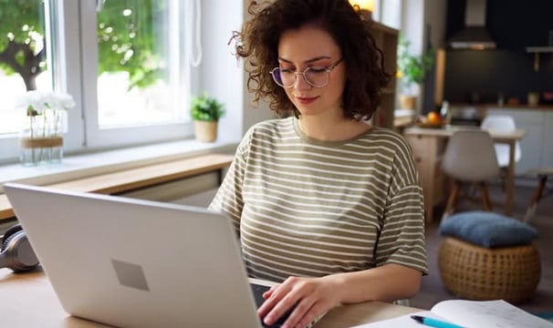 uma mulher de óculos, cabelos ondulados, mexendo em um notebook