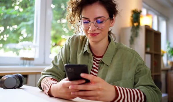 uma mulher de óculos, cabelos ondulados, mexendo em um celular