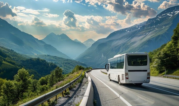 A white color bus travelling in a valley surrounded by mountains and greenery