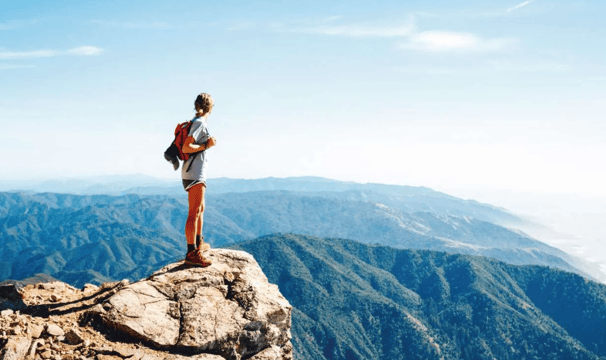 A women standing on a mountain rock and observing the beautiful view of a valley